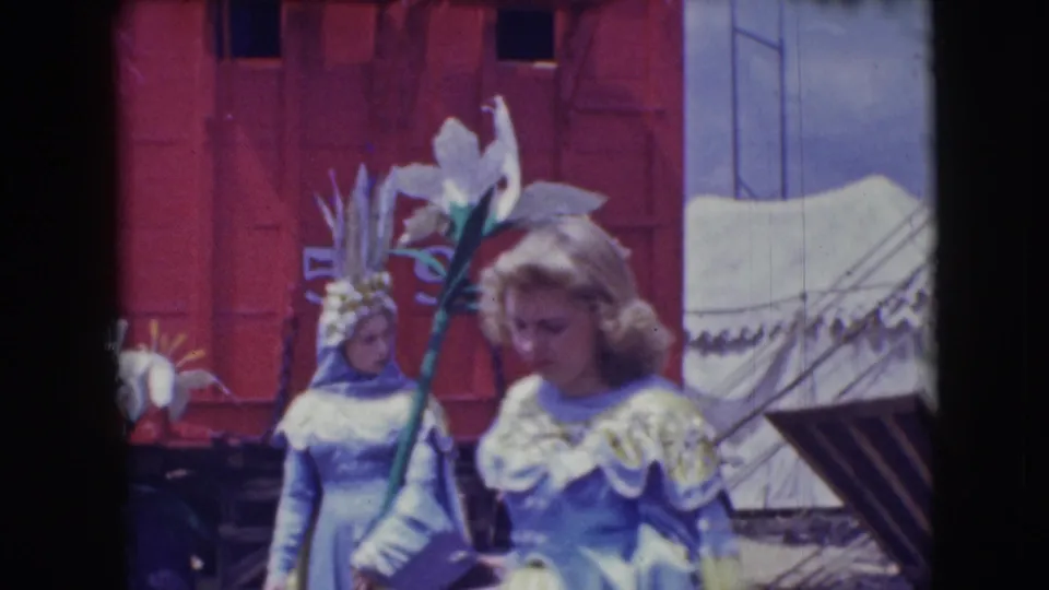 At the 1948 Sarasota circus, a woman in a pale blue ruffled dress stands near another costumed performer and tent canvas.