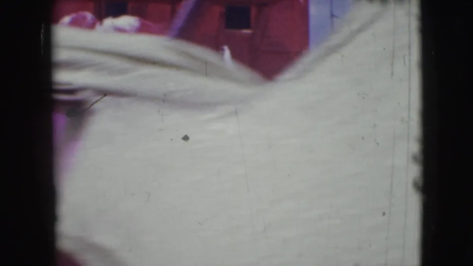 Soft 8mm frame from the Sarasota clip with pale costume fabric close to the lens, dark gate edges and a red backdrop behind it.