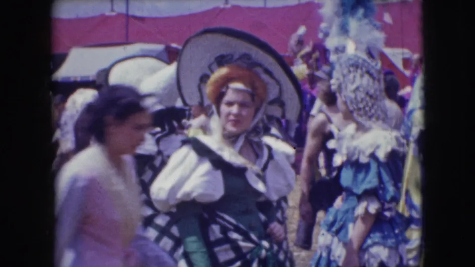 Costumed adults at the Sarasota Ringling Brothers event, with large hats, feathered decoration and a blurred passerby in the foreground.
