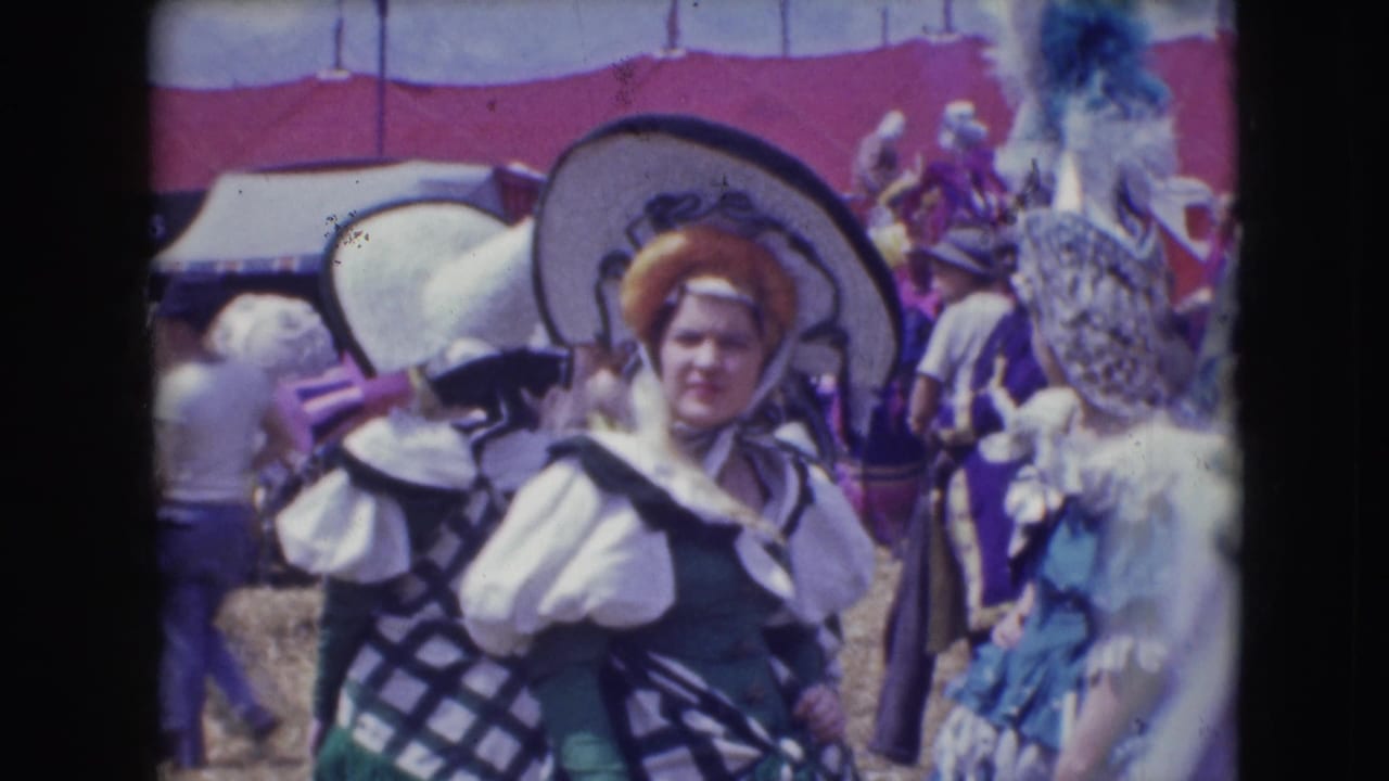 1948 Sarasota circus footage shows costumed participants in wide hats and feathered headpieces standing in a crowded outdoor area.