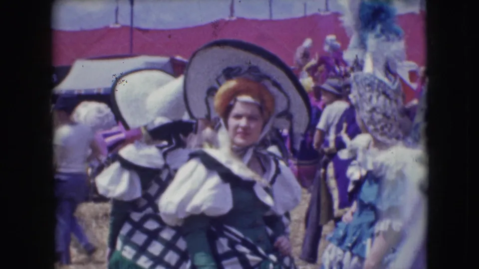 1948 Sarasota circus footage shows costumed participants in wide hats and feathered headpieces standing in a crowded outdoor area.
