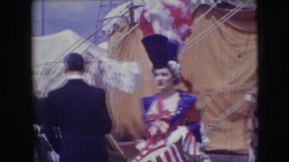 A costumed performer wearing a tall feathered hat and red, white, and blue outfit stands near tent canvas in the 1948 circus scene.