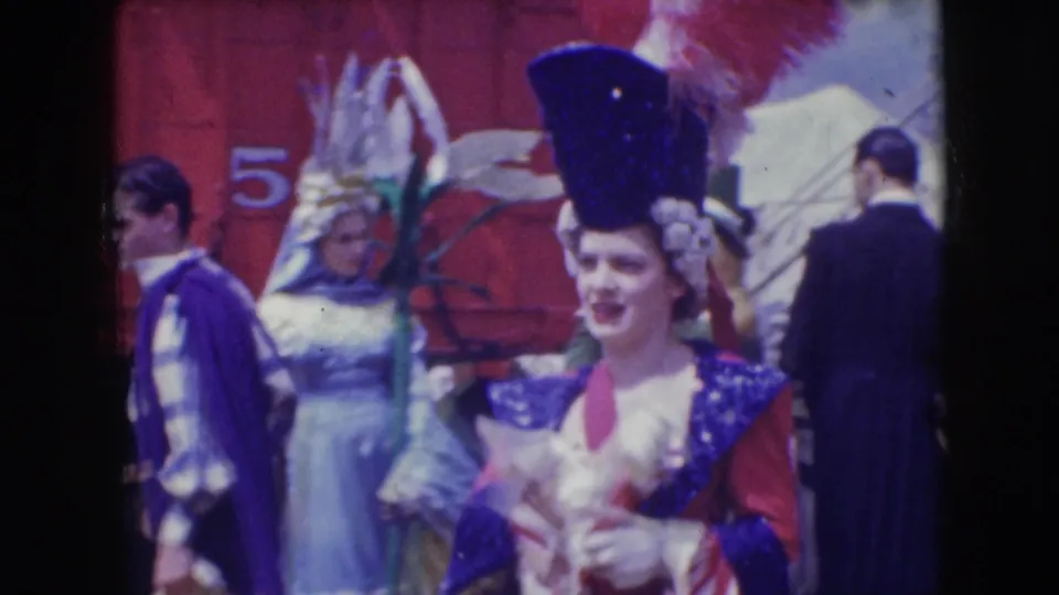 Costumed performers in tall hats and colorful outfits pass in front of a red backdrop during the Sarasota Ringling Brothers scene.