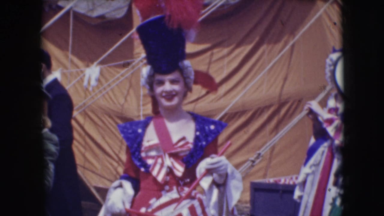 At Ringling Brothers in Sarasota in 1948, a woman in a red, white, and blue circus costume smiles near tent rigging while holding drumsticks.