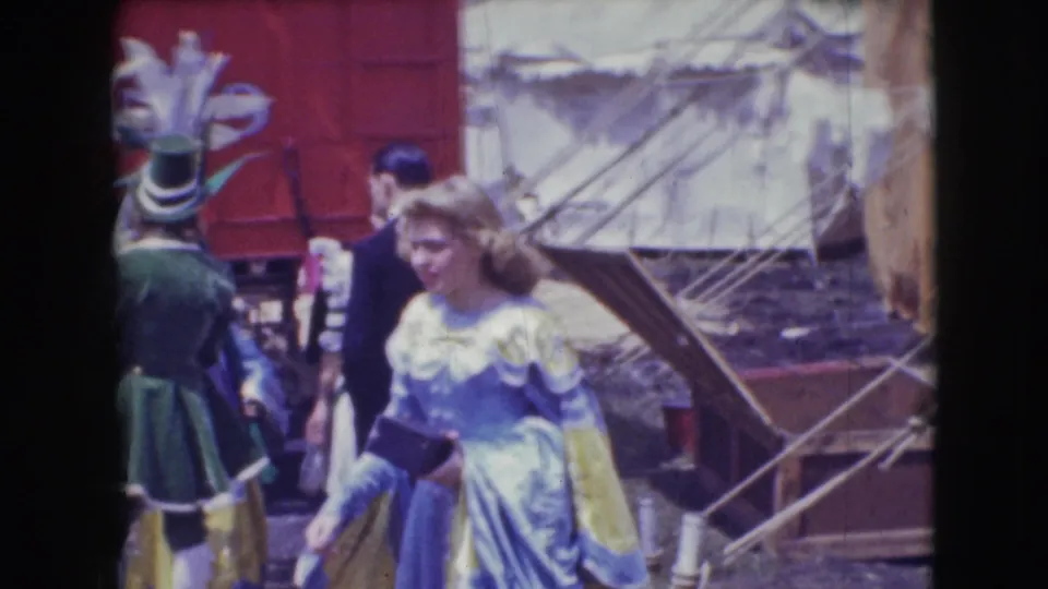 A green-and-yellow costumed circus figure and a woman in a pale dress appear near tent rigging and canvas structures in Sarasota in 1948.