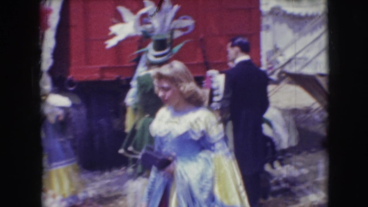 1948 Sarasota circus scene with a woman in a blue and yellow costume walking near a horse, red wagon, and other performers.