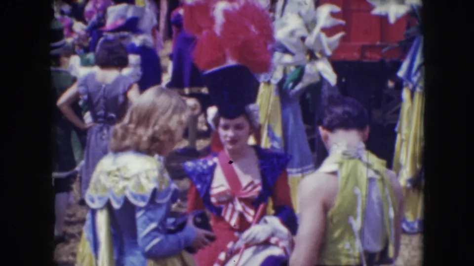 A woman in a red and blue circus costume stands amid other 1948 Sarasota performers in feathered hats and pastel dresses.