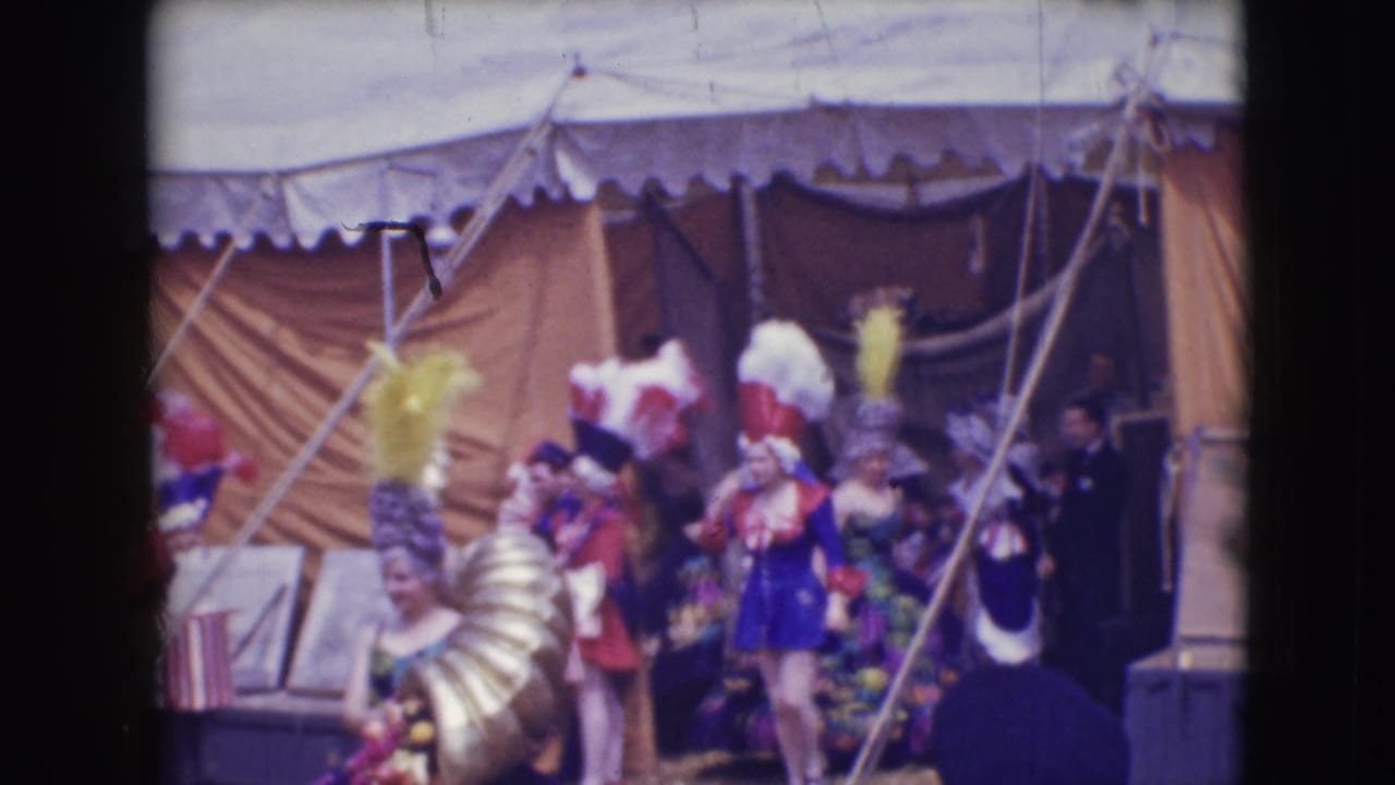 1948 Sarasota circus performers in colorful feathered headpieces and costumes gather near canvas tent walls before a show.