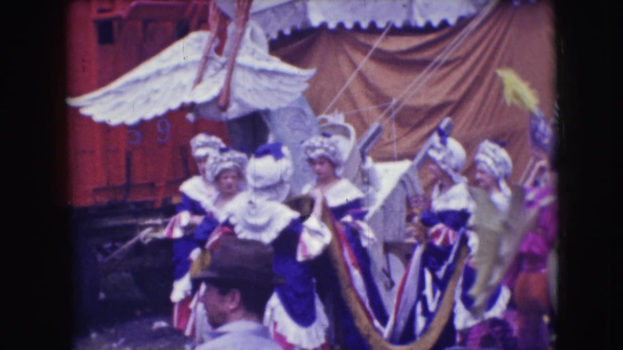 1948 Sarasota circus parade frame with white and blue feathered performers near a horse, a red rail car, and tent fabric.