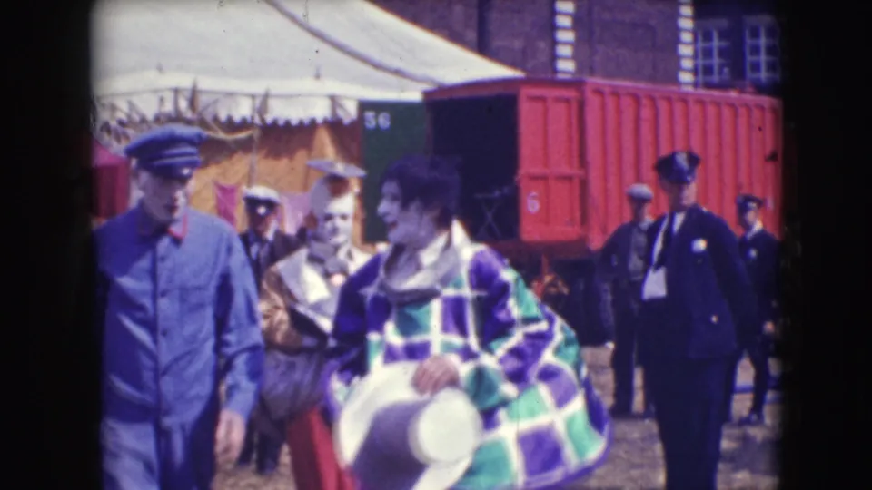 Clowns and uniformed circus staff move across the 1948 Sarasota lot, with canvas tents and a red rail car visible behind them.
