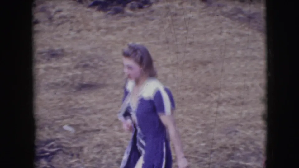 1948 Sarasota circus-event home-movie frame showing a woman in a purple and white dress walking across hay-covered ground.