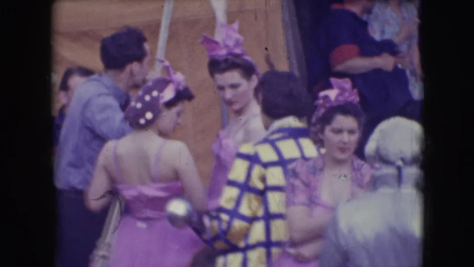 Adults in circus costumes and performance clothing stand close together during a brief backstage break in the 1948 Sarasota footage.