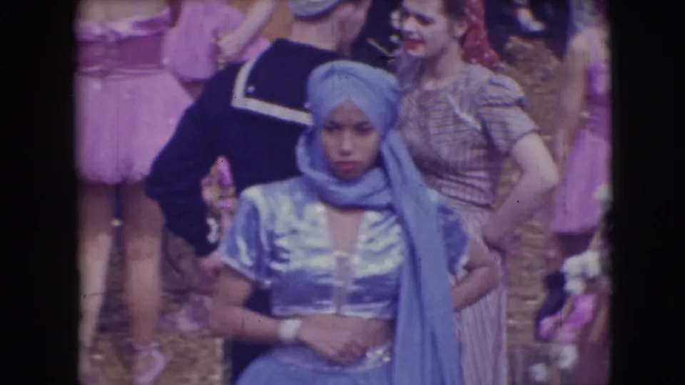 A woman in a blue satin costume and matching headscarf stands in front of other adult performers in the 1948 Sarasota circus footage.