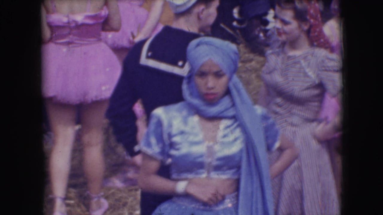 Costumed performers stand together, with a blue turbaned performer centered near a sailor uniform and pink tutu.