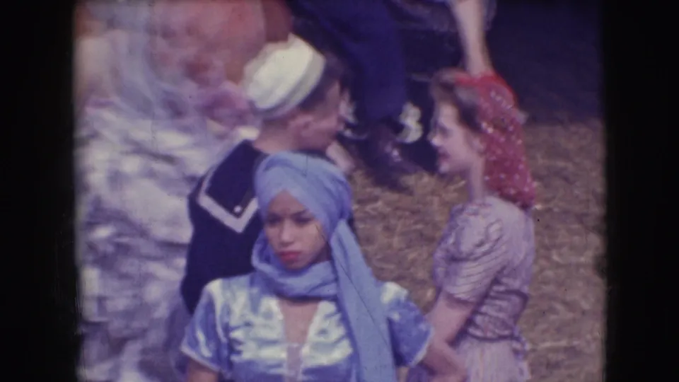 A 1948 circus home-movie frame shows the blue-costumed performer in the foreground with other performers conversing behind.