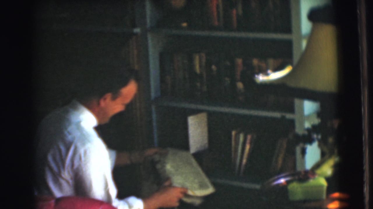 The seated man lowers his gaze to an open newspaper, with bookshelves and a lamp visible in the 1951 home interior.