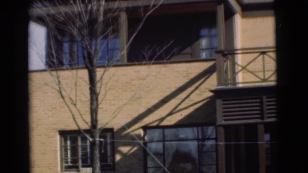 1951 Chatham, New Jersey 8mm frame showing a tan brick building facade with balcony railings, windows, tree branches, and strong shadows.