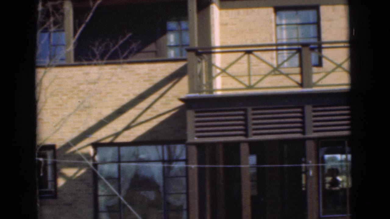 Brick facade with balcony railing, louvered panel, tall windows, and deep shadows at the frame edges.