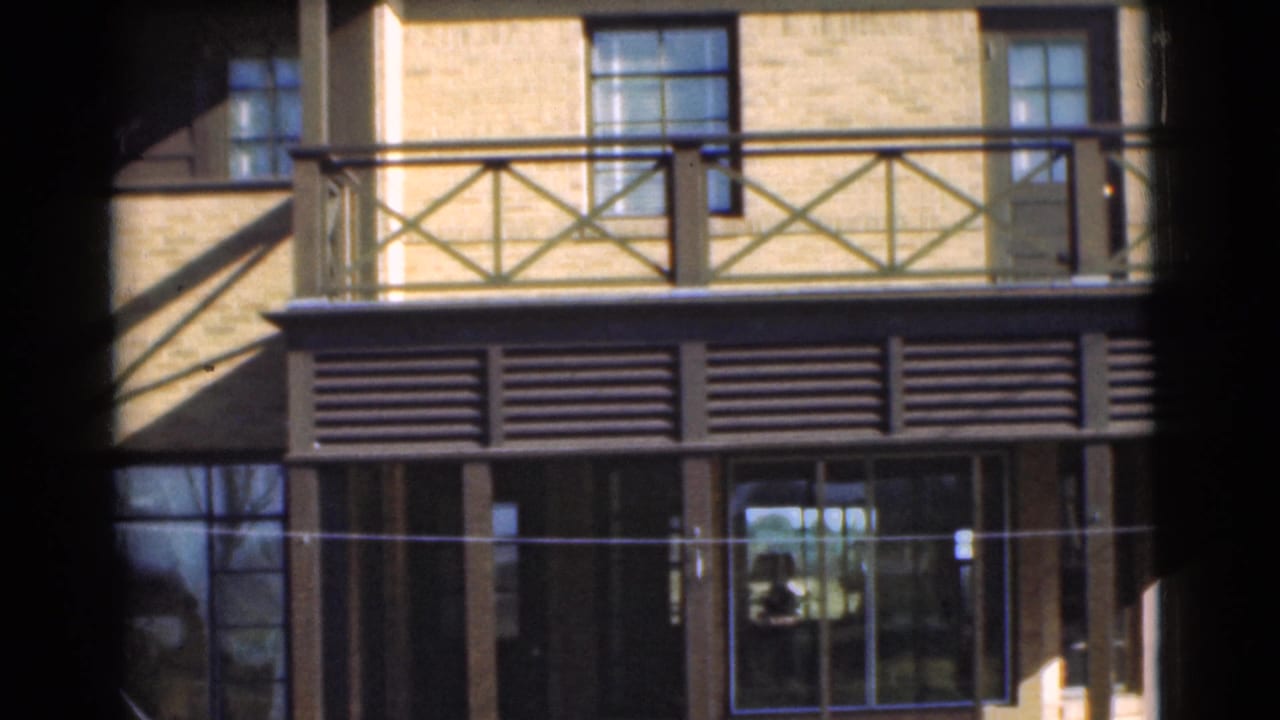 1951 Chatham, New Jersey 8mm frame showing balcony railings, louvered panels, brickwork, windows, and glass doors in bright sun.