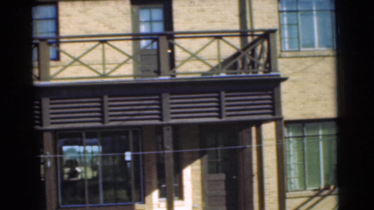 1951 Chatham, New Jersey home-movie frame showing a yellow brick residential facade with a dark balcony and louvered awning.