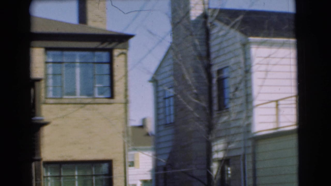 1951 Chatham frame showing the edge of a yellow brick building next to a white clapboard house, with bare branches in front.