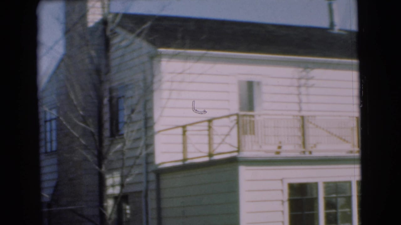 1951 Chatham home-movie frame of a white clapboard house with a small balcony, simple railing, windows, and branches.