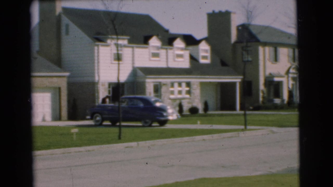 1951 Chatham, New Jersey frame with a white two-story home, attached garage, dormer windows, lawn, bare tree, and dark sedan near the curb.