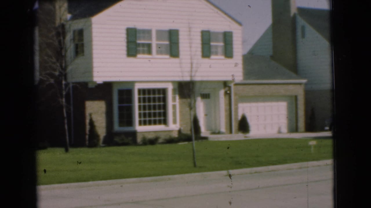 1951 Chatham, New Jersey home-movie frame showing a white two-story suburban house with green shutters, lawn, driveway, and sidewalk.
