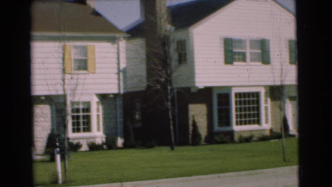 1951 Chatham, New Jersey frame of a residential house front with pale siding, shutters, lawn, mailbox, and part of a neighboring home.