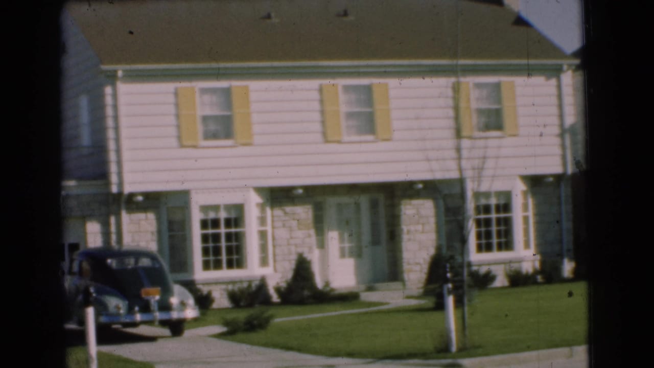 1951 Chatham, New Jersey frame showing a suburban house front, pale shutters, lawn, mailbox, sidewalk, and a dark rounded car parked in the driveway.