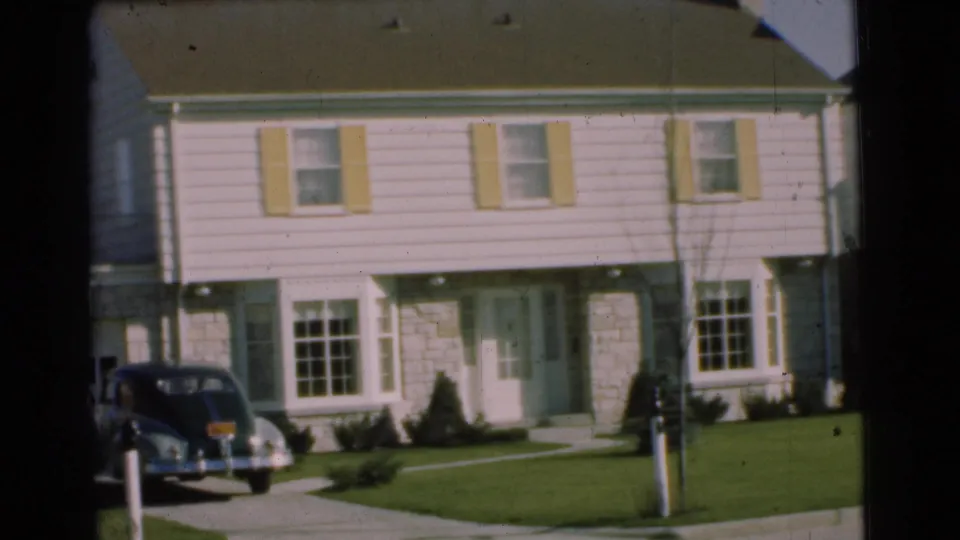 1951 Chatham, New Jersey frame showing a suburban house front, pale shutters, lawn, mailbox, sidewalk, and a dark rounded car parked in the driveway.