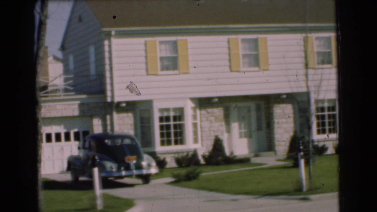 1951 Chatham, New Jersey home-movie frame showing a light house, yellow shutters, garage, lawn, and dark sedan in the driveway.