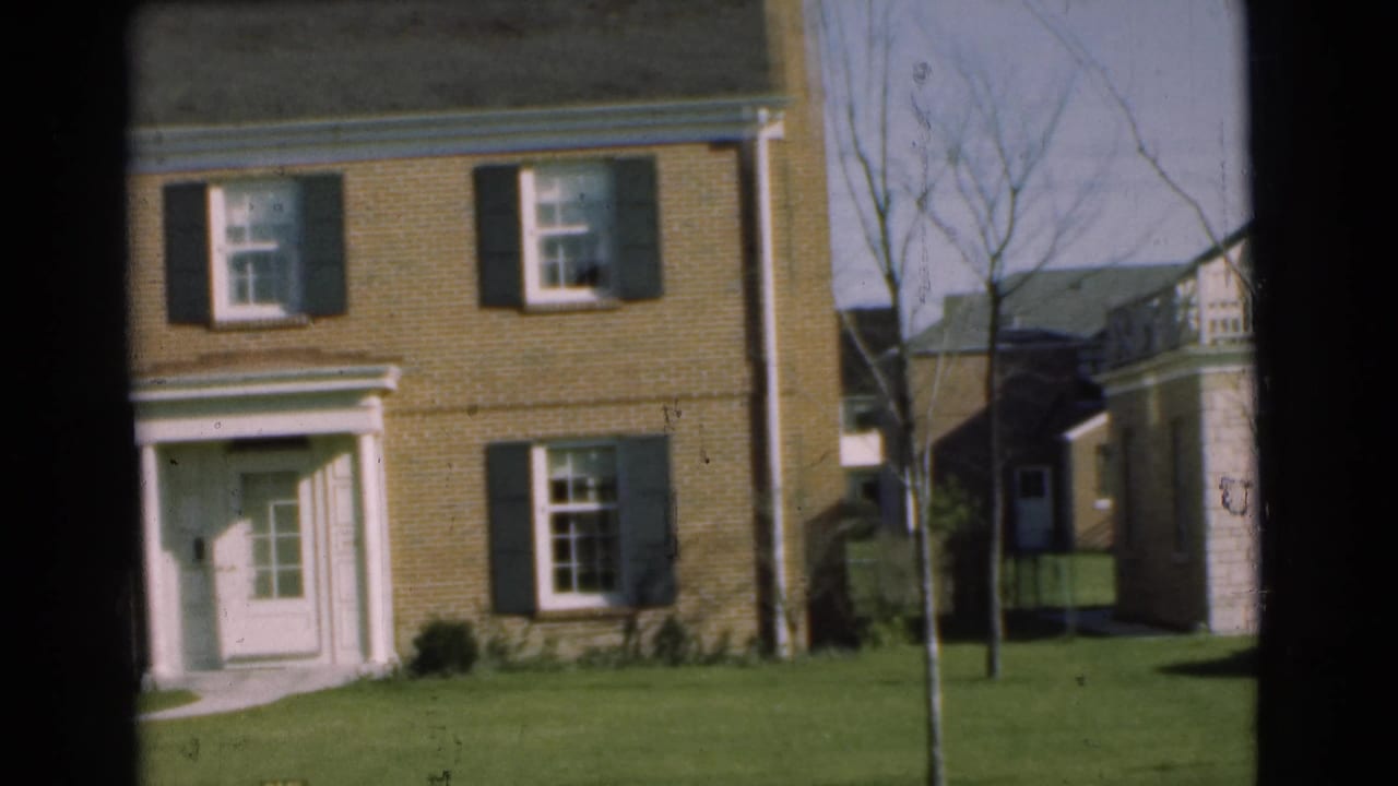 1951 Chatham residential street view showing a brick house with dark shutters, a doorway, lawn, bare trees, and neighboring siding.