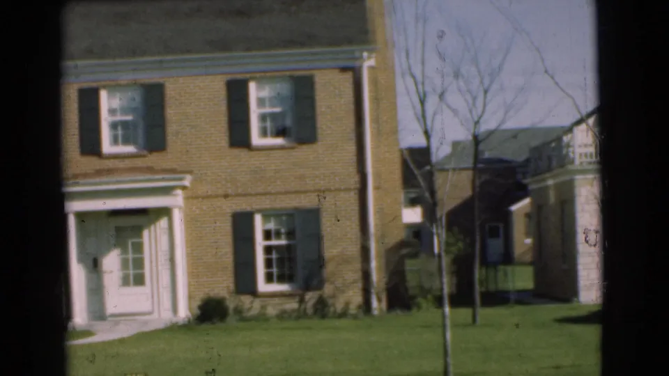 1951 Chatham residential street view showing a brick house with dark shutters, a doorway, lawn, bare trees, and neighboring siding.