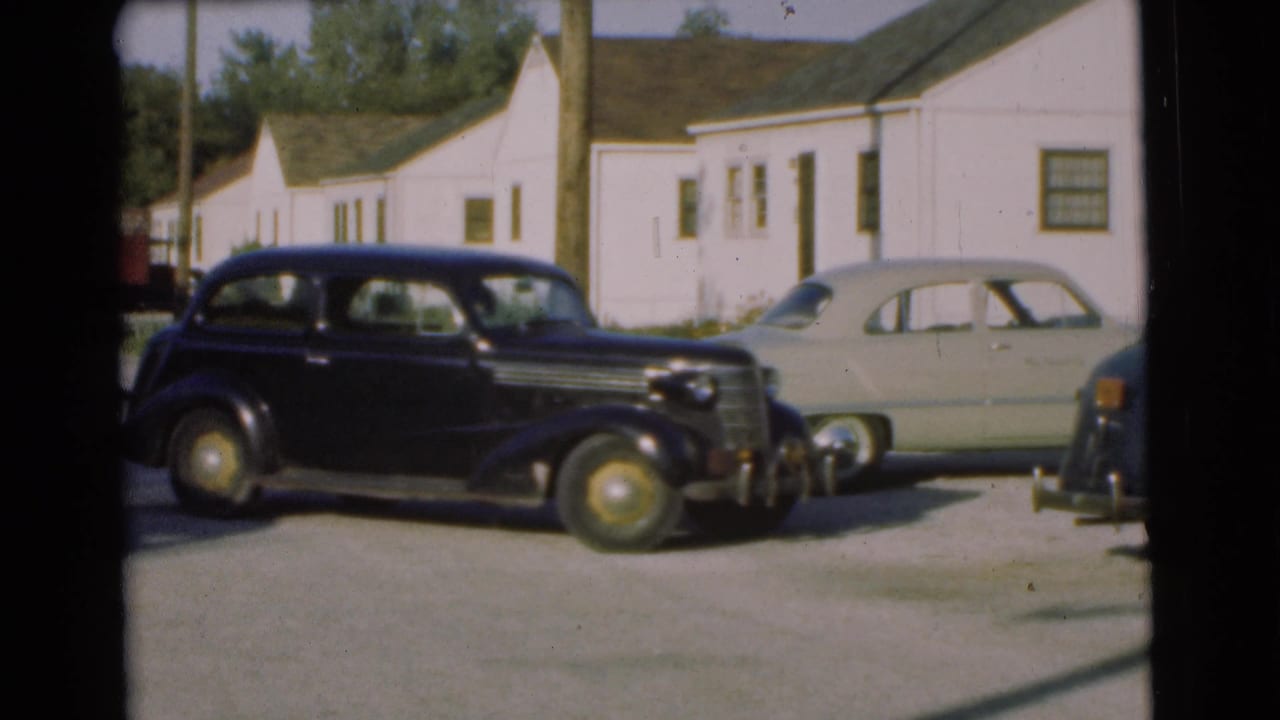 1951 Chatham, New Jersey home-movie frame showing a black sedan near a pale parked car and white clapboard houses.