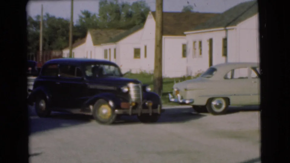 The black sedan moves through the Chatham parking area, passing a utility pole and a pale parked mid-century car.