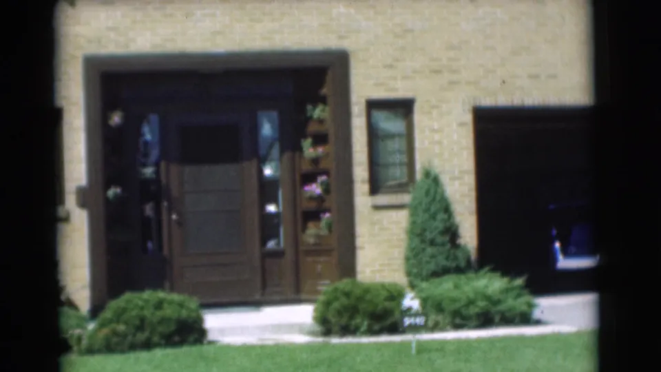 1951 Chatham, New Jersey frame showing the brick house entry, dark doorway area, plant shelves, lawn, windows, and trimmed greenery.