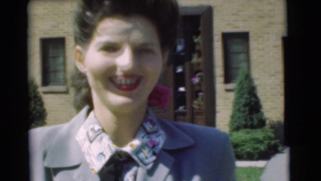 Close view of a smiling woman standing before a house entrance and lawn.