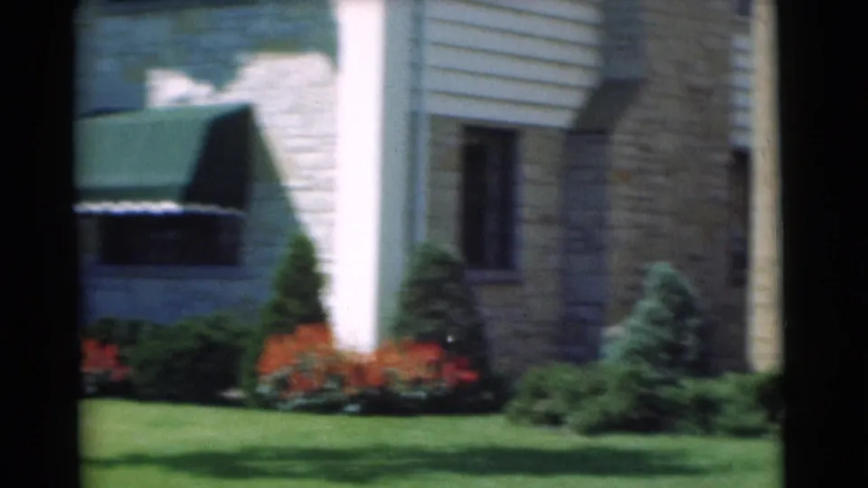 A brief exterior view shows part of the Chatham residence, with lawn, shrubs, red flowers, siding, stone or brickwork, and a dark awning.