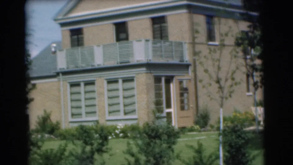 1951 Chatham, New Jersey 8mm frame showing a closer view of a brick facade with balcony, shuttered windows, door, lawn, and plantings.