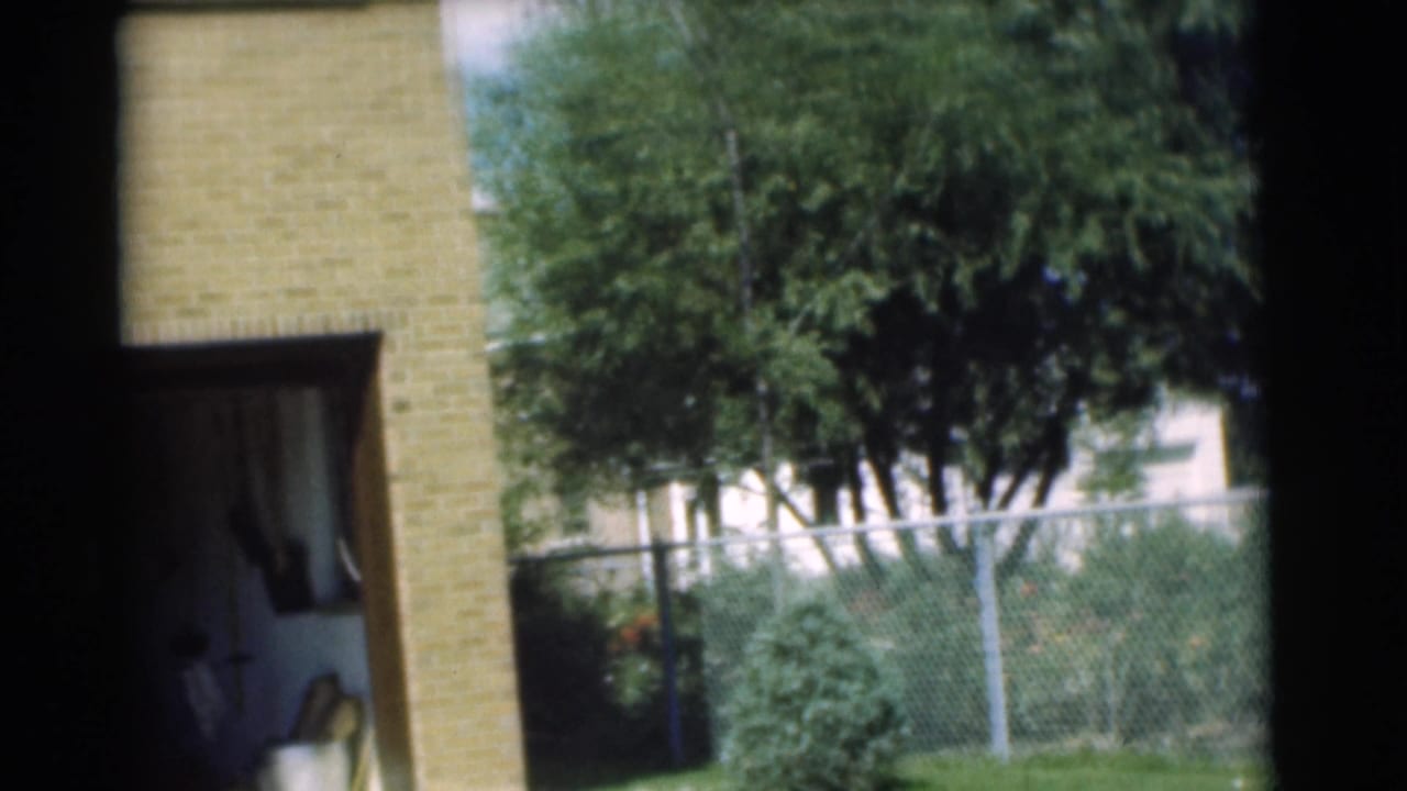Open garage in a tan brick house with trees and fence visible nearby.