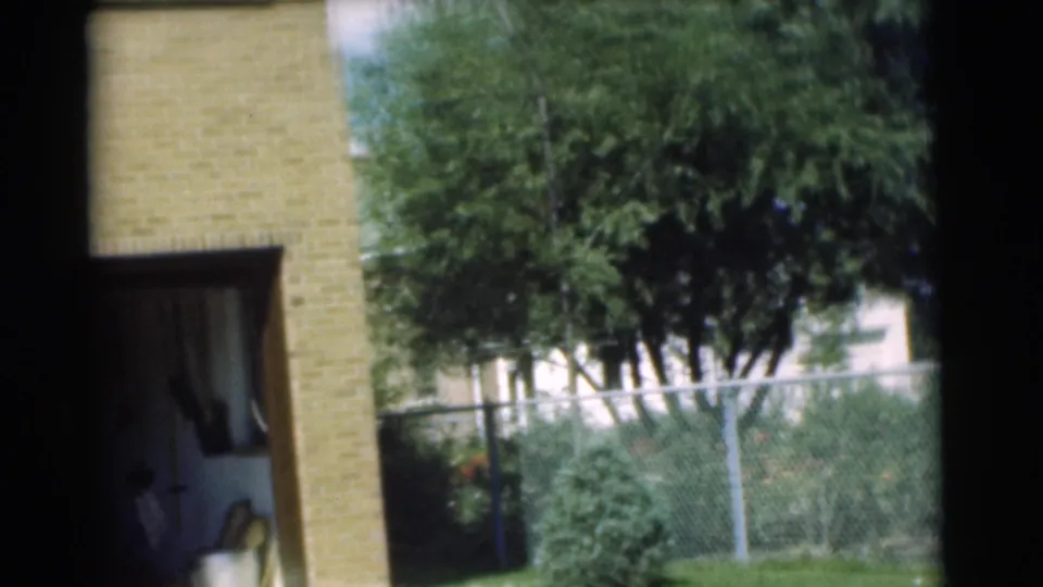 1951 Chatham, New Jersey frame showing an open garage in a tan brick house with trees and a chain-link fence beside it.
