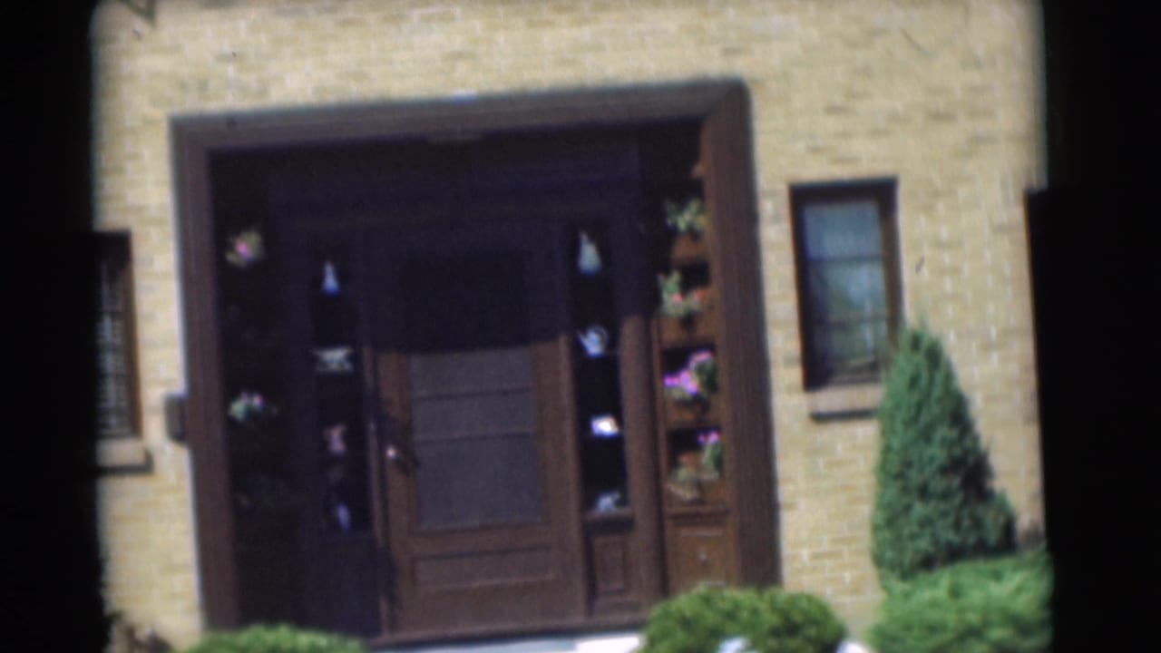 Closer view of the brick house entrance with dark wood surround, flower boxes, shrubs, and a side window.