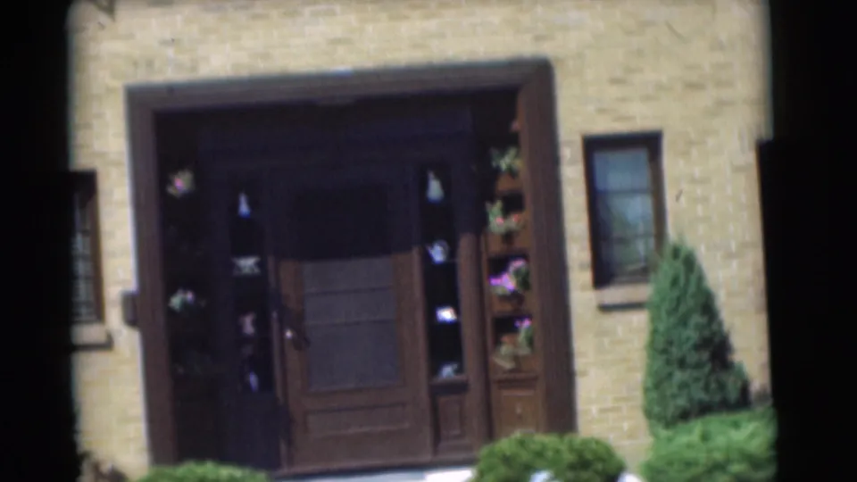 1951 Chatham, New Jersey frame centered on the house's dark wood front entrance, flanking display shelves or flower boxes, shrubs, and brick wall.