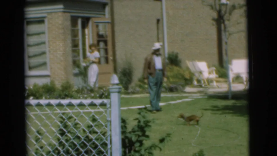 1951 Chatham, New Jersey frame with a woman by the back door, a man on the lawn, and a small puppy near a chain-link fence.