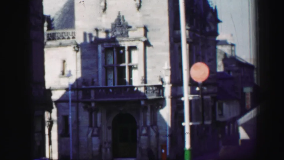 1952 Edinburgh street-level view of an ornate stone facade with arched entrance, balcony rail, lamppost, and red circular traffic sign.