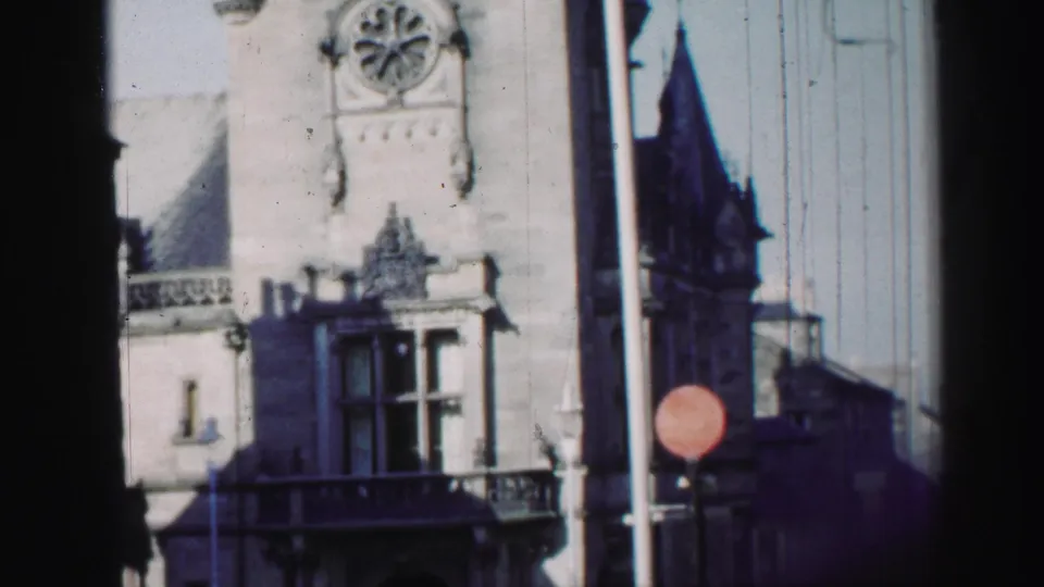 1952 Edinburgh frame showing a higher portion of the ornate stone facade, including circular window detail above the balcony and street sign.