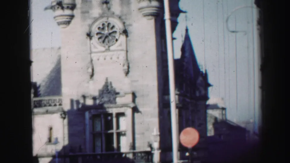 1952 Edinburgh upper facade detail with circular window, carved ornament, lamppost, red traffic sign, and adjacent dark roofline.