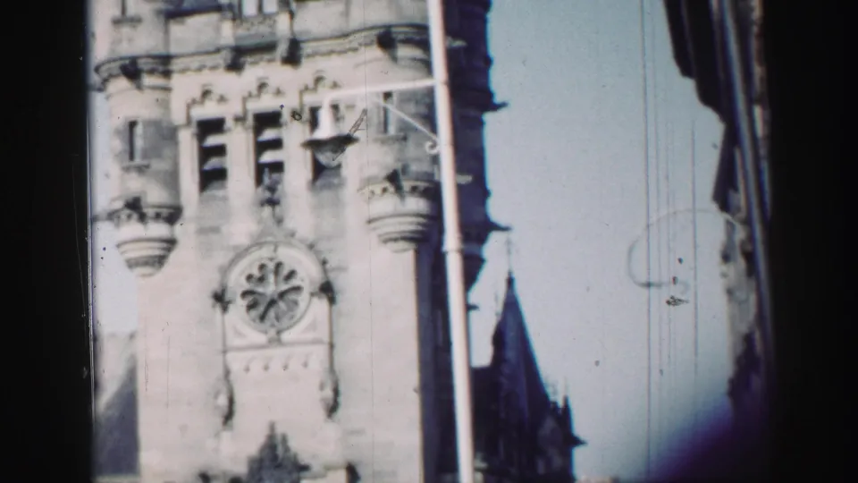1952 home-movie frame of the Edinburgh Gothic Revival facade, showing the clock face, upper windows, and framing edges.