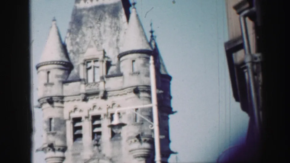 1952 Edinburgh 8mm view of the church tower's upper stonework, turrets, and decorative openings under a pale sky.
